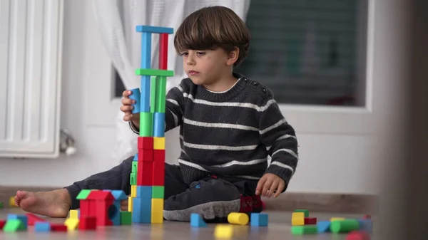 Child building tower with colorful blocks. One small boy playing in bedroom floor. Candid lifestyle childhood creative development