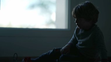 Karanlıkta oturan bunalımlı bir çocuk. Yalnız küçük çocuk pencerenin yanında yerde yatıyor. Hüzünlü zorba çocuğun silueti