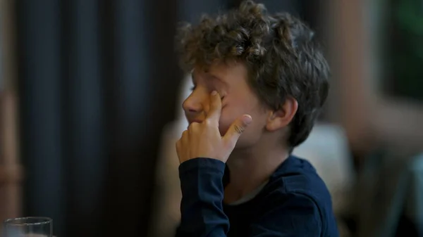 Young boy scratches eye with finger