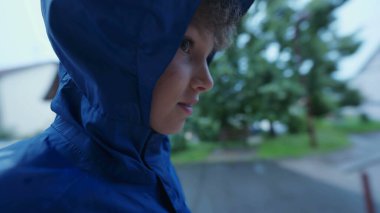 Yağmurlu bir günde sokakta yürürken mavi yağmurluk giyen çocuk yüzü. Erkek çocuk yağmurdan korunmak için su geçirmez ceket giyiyor.