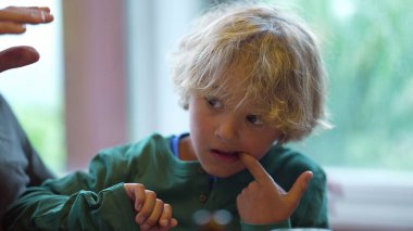 Ağzında parmağı olan bir çocuk dişlerinden bir parça yiyecek çıkarmaya çalışıyor.