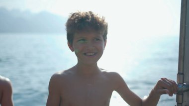 Yakışıklı genç erkek çocuk gölün kenarında duruyor. Sahilde güneşlenen üstsüz küçük çocuk.