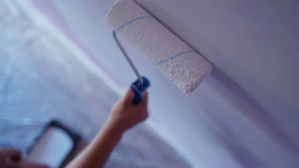 Closeup paint roller on wall. Worker painting house remodeling. Person hands renovating painting house