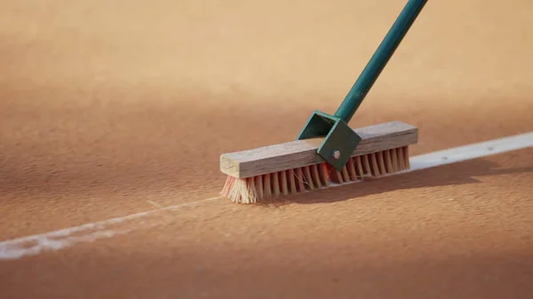 Cleaning marking line clay tennis court with brush. Clay tennis court cleaning. Maintenance and preparation surface of orange sport ground game
