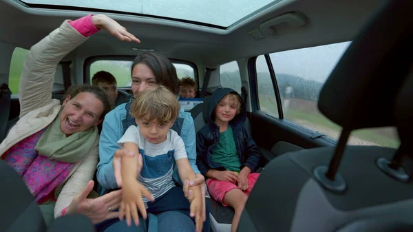 Happy people inside car backseat waving hands laughing and smiling together. Family traveling in vehicle interior on road. Authentic happiness concept