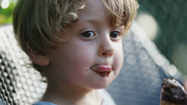 Adorable child boy with dirty mouth covered with chocolate ice cream. Messy kid outside. Contemplative pondering question