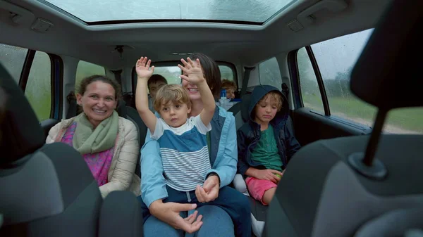 Happy people inside car backseat waving hands laughing and smiling together. Family traveling in vehicle interior on road. Authentic happiness concept