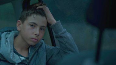 Yağmurlu bir günde araba arka koltuğunda yolculuk eden dalgın bir genç çocuk. Çocuk aracın içinde seyahat ediyor.