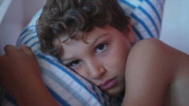 Üzgün, genç bir çocuk. Kapalı bir yüz. Yastığa uzanmış düşünüyor. Bunalımlı erkek çocuk. Küçük çocuk duygusal acı çekiyor.