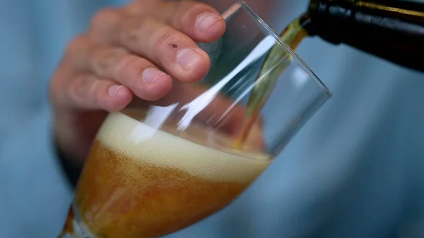 Pouring beer into glass closeup in slow motion. Closeup hand serving beer into glass