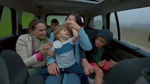 Happy people inside car backseat waving hands laughing and smiling together. Family traveling in vehicle interior on road