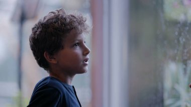 Pencere kenarında dikilip bakan düşünceli bir çocuk