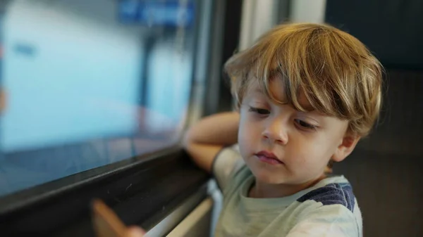 One small boy traveling by train seated by window. Child inside moving transportation. Closeup kid face