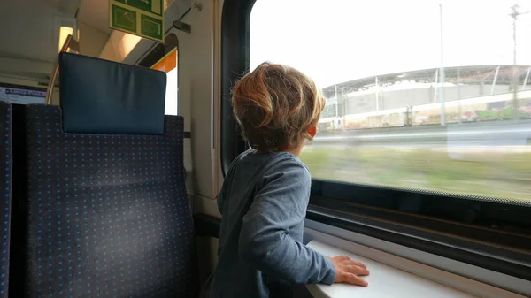 Little boy traveling by train staring outside through transportation window