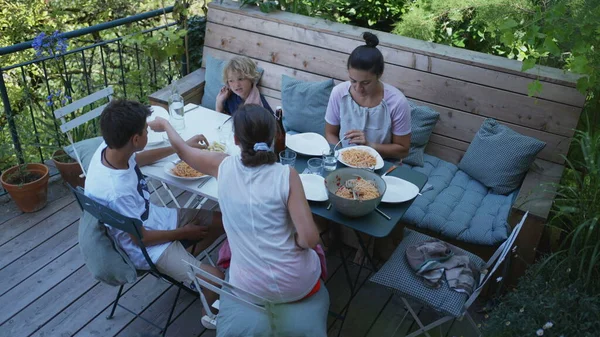 People eating lunch at house wooden patio outdoors. Children and two women eat meal