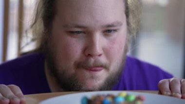 Overweight Person wanting to eat sugar food on plate. One Young fat man in diet fasting from junk food. Donut closeup in front of fat guy. Weight loss concept