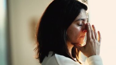 Depressed woman suffering from mental illness at home. Female person with preoccupied expression standing by window