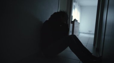 One anxious depressed woman covering face in despair sitting at home in the dark. Person suffering alone in corridor feeling shame and regret