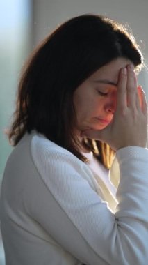 One worried woman standing by window with pensive preoccupied expression. Thoughtful anxious emotion of a female person thinking about problem. Vertical Video