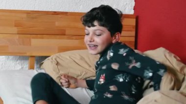 One small boy waking up in the morning getting out of bed. Child wearing pajamas removing duvet bedsheets. Kid starting the day