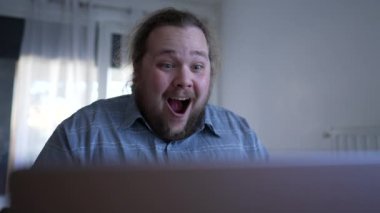 One happy man celebrates success in front of computer. A male chubby entrepreneur kissing laptop screen overjoyed by excellent news