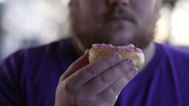 Closeup hand holding donut with chubby man in mouth wanting to eat junk food