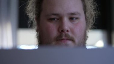 Close up face man working in front of computer screen with serious expression. Concentrated male person staring at laptop focused on task