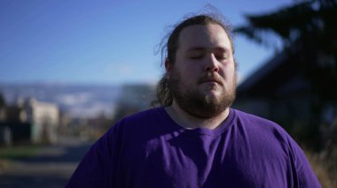 One calm man meditating outside. A chubby guy portrait with eyes closed relaxing outdoors in contemplation. Tracking shot