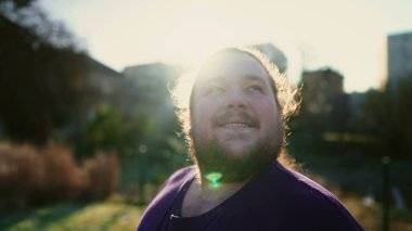 joyful overweight young man standing outdoors looking at sky with hope