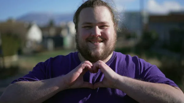One young overweight man doing heart sign with hands outside. Happy chubby person doing love symbol expressing caring