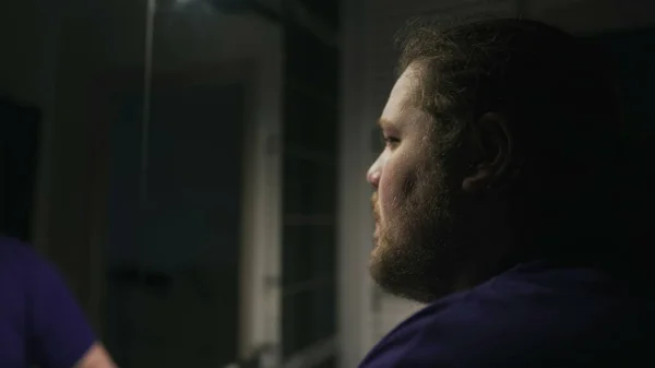 One overweight person suffering alone in front of bathroom mirror. Depression concept of a chubby man facing himself in front of mirror during hard times