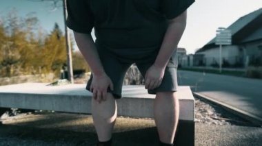 Person suffering from knee pain getting up from park bench outdoors. Man with hand feeling leg injury