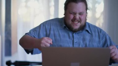 Young man winning something online. One happy fat casual person celebrates news in front of laptop computer feeling excitement. Winner concept