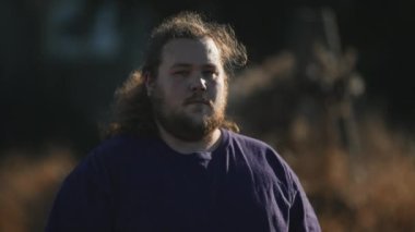 One overweight young man standing outdoors looking at camera with serious casual expression