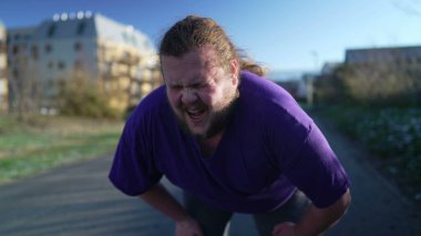 A fat young man taking a break from run. One overweight person recovering from exercising outdoors. Motivational discpline back into shape concept. Guy resting