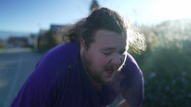 A fat young man taking a break from run. One overweight person recovering from exercising outdoors. Motivational discpline back into shape concept. Guy resting