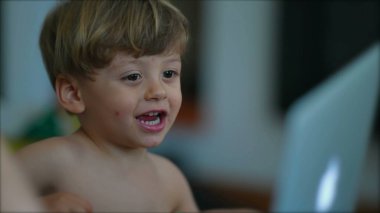 Çocuk ailesiyle birlikte bilgisayara bakıyor. Anne eli bebek bebekle ekranı işaret ediyor. Bilgisayarın önünde içeriğe bakan çocuğun yakın çekim yüzü.