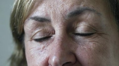 Portrait face close up of a senior woman opening eyes at camera with happy expression. Macro eyes of a mature female person in 70s