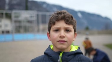 Parkın dışında kameraya bakan ciddi bir gencin portresi. Kışlık ceket giyen endişeli bir çocuk.