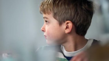 Candid thoughtful young boy closeup face. One pensive child thinking while sitting at lunch table eating meal