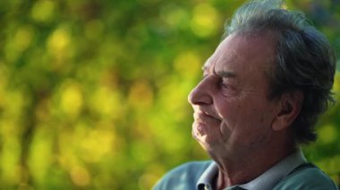 A thoughtful senior man sitting outside at park in deep contemplation. Candid close up of a pensive mature older person in nature