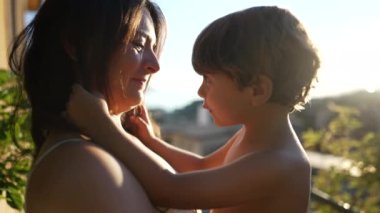 Joyful mother holding baby child son in arms during beautiful sunset time. Parent bonding with kid during golden hour moment