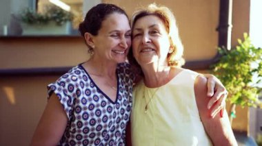 Happy adult daughter posing with older mother. Portrait of two women smiling together in embrace during sunny daylight outdoors