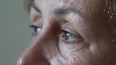 A thoughtful senior woman with contemplative expression macro eyes close up. One mature older female person in 70s looking at horizon daydreaming