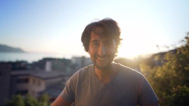 Portrait of a happy man in 30s standing outdoors in sunset time overlooking landscape in background. Close up face male person