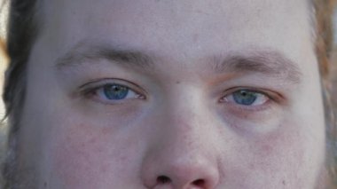 Young man macro blue eyes close up looking at camera with serious expression. A caucasian male person extreme eye closeup