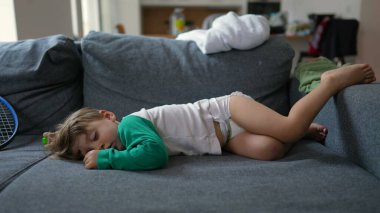 Küçük komik çocuk öğleden sonra uykusunda kanepede uzanıyor. Bebek bebek bezi takmış, kanepede uyuyor.