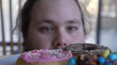 Chubby man tempted to eat junk food on plate. A fat male person wanting to eat donuts. Sugar carb food temptation