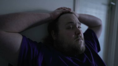 One pensive overweight suffering from anxiety sitting at home in the dark. Close up face of a preoccupied male person