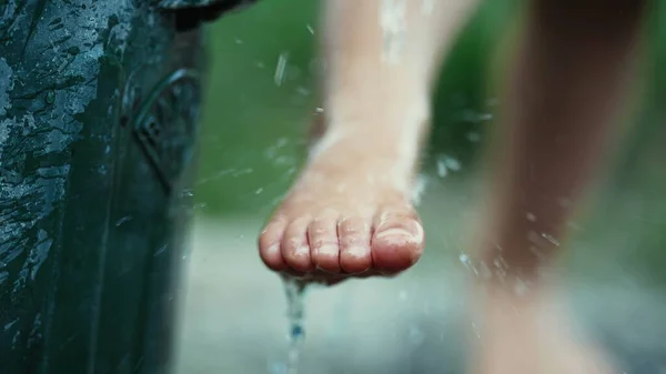 Child cleaning foot at water faucet outdoors. Kid cleaning body feet at park